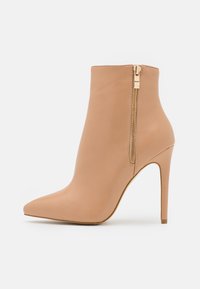 Beige Knöchelstiefel aus glattem Leder mit spitzer Zehe, hohem Stiletto-Absatz und goldfarbener Reißverschlussdetail an der Seite.