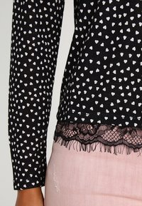 Czarny top z długim rękawem w biały wzór serc z czarną koronkową falbaną w połączeniu z jasnoróżowymi spodniami z lekkim przetarciem.