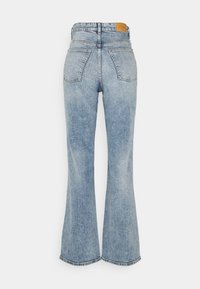 Jeans acampanados de color azul claro fabricados en denim, con cintura alta, dos bolsillos traseros y un parche de cuero en la cintura.