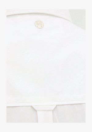 Tessuto bianco con bordo cucito e un emblema metallico rotondo etichettato "SAFARI BEACH" vicino al centro superiore.