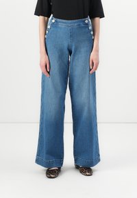 Helleblaue, weite Jeans mit hoher Taille, ausgestattet mit großen silbernen Knöpfen an der Seite und einer klaren, geraden Silhouette.