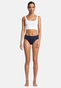 Weißes Baumwoll-Crop-Top mit breiten Trägern, kombiniert mit marineblauen, hochgeschnittenen Bikini-Höschen, beide aus einem glatten Material mit minimalistischem Design.