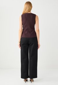 Mouwloos donker bordeaux topje met een getailleerd ontwerp, gecombineerd met hoge taille zwarte wijd uitlopende broek en zwarte hoge hakken.