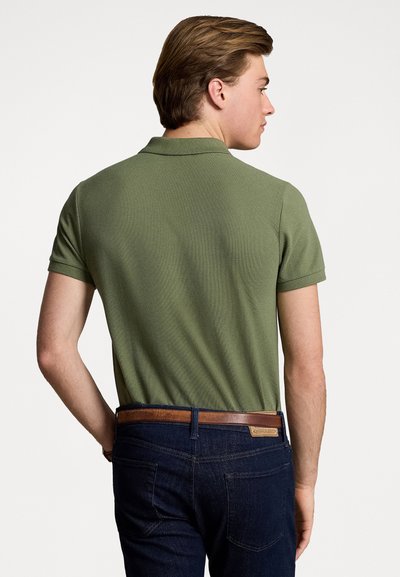 Cămașă polo de culoare verde măsliniu, realizată dintr-un material texturat, cu guler clasic și mâneci scurte, asortată cu blugi negri și o curea maro.