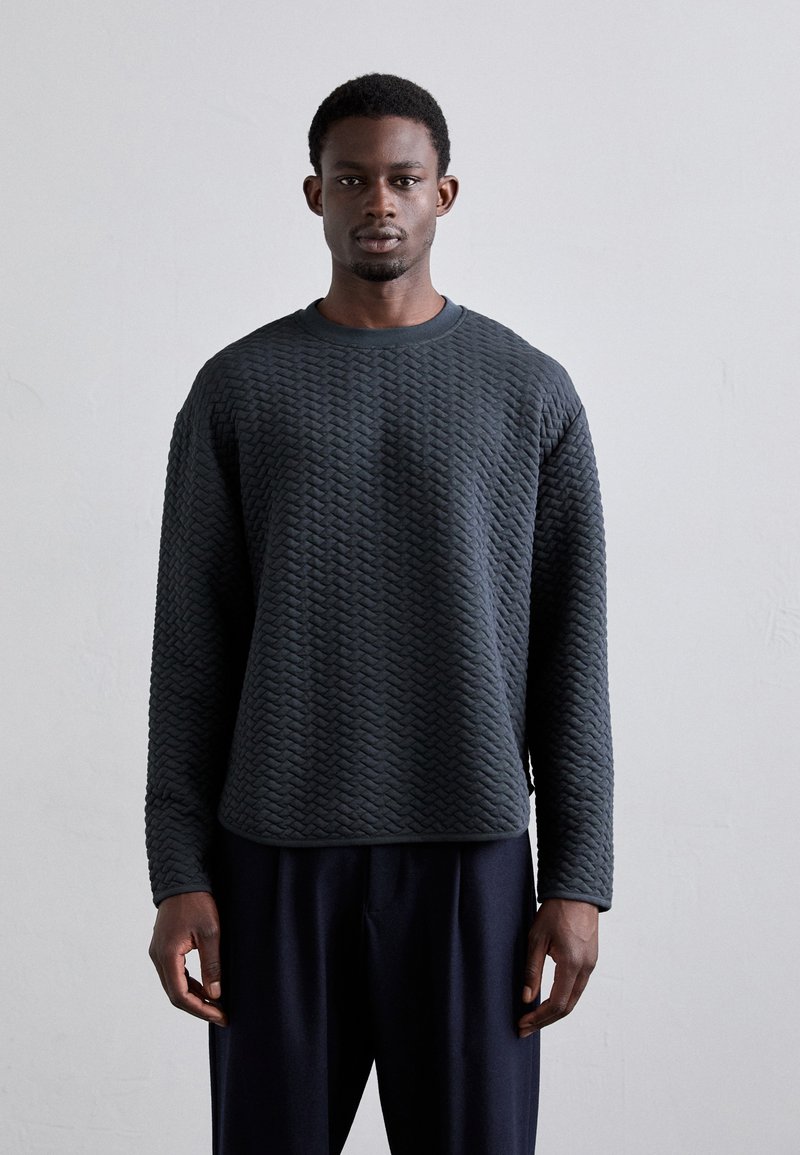 Sweatshirt matelassé gris foncé avec un col rond et des manches longues, présentant un motif tissé texturé et une coupe décontractée.