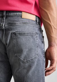Šedé džíny z denimu s texturovaným povrchem, se značkovou koženou nášivkou, zadními kapsami a kontrastními švy.