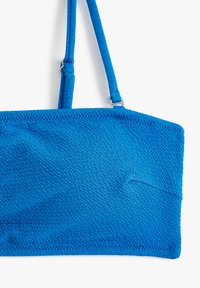 Lyst blå bikini top med tekstureret stof, rektangulær form, justerbare stropper og stikninger langs kanterne.