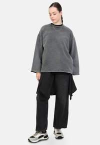 Overmaatse grijze sweaters, losse zwarte broeken met een gestreept detail, en beige sneakers met zwarte accenten. Eenvoudige ketting inbegrepen.