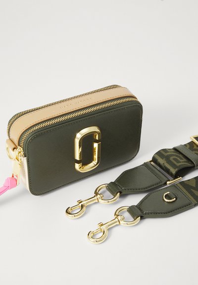 Green and beige rectangular bag with a gold zipper and logo. Features a detachable green camo strap with gold clips and a pink accent.