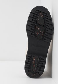 Suela de goma negra con superficies texturizadas y manchas naranjas, que presenta el logo de la marca en relieve. Bisel superior de color claro y suave visible.
