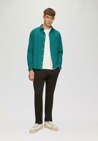 Turquoise gemusterde overhemddas over een wit t-shirt, gecombineerd met zwarte broek en beige sneakers. Gladde stof met gedetailleerd ontwerp.