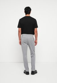 Grijze broek met een gladde textuur, voorzien van een rechte pootontwerp en twee achterzakken. Gecombineerd met een zwart t-shirt met korte mouwen.