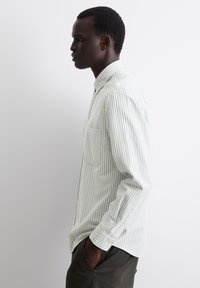 Light green striped button-up shirt with a chest pocket, textured fabric, and long sleeves, worn with dark-colored pants.