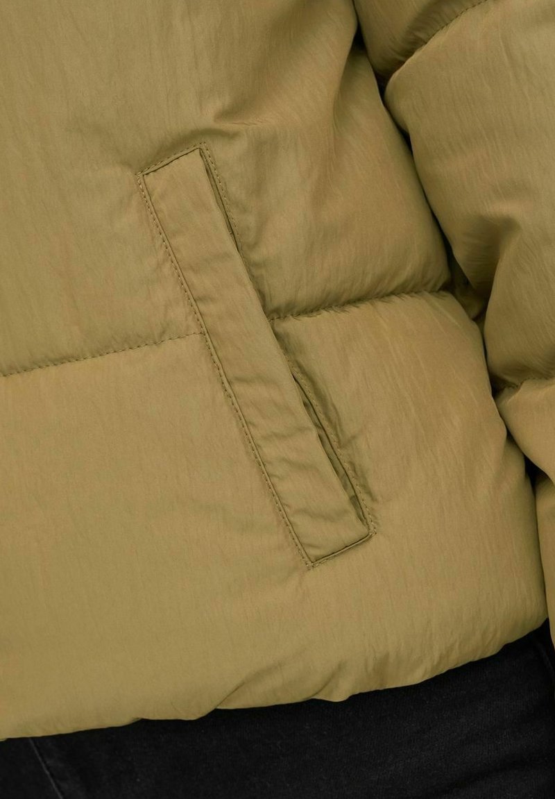 Cazadora acolchada en verde oliva con una textura lisa y brillante, que presenta un bolsillo lateral con un detalle de costura y un diseño acolchado.