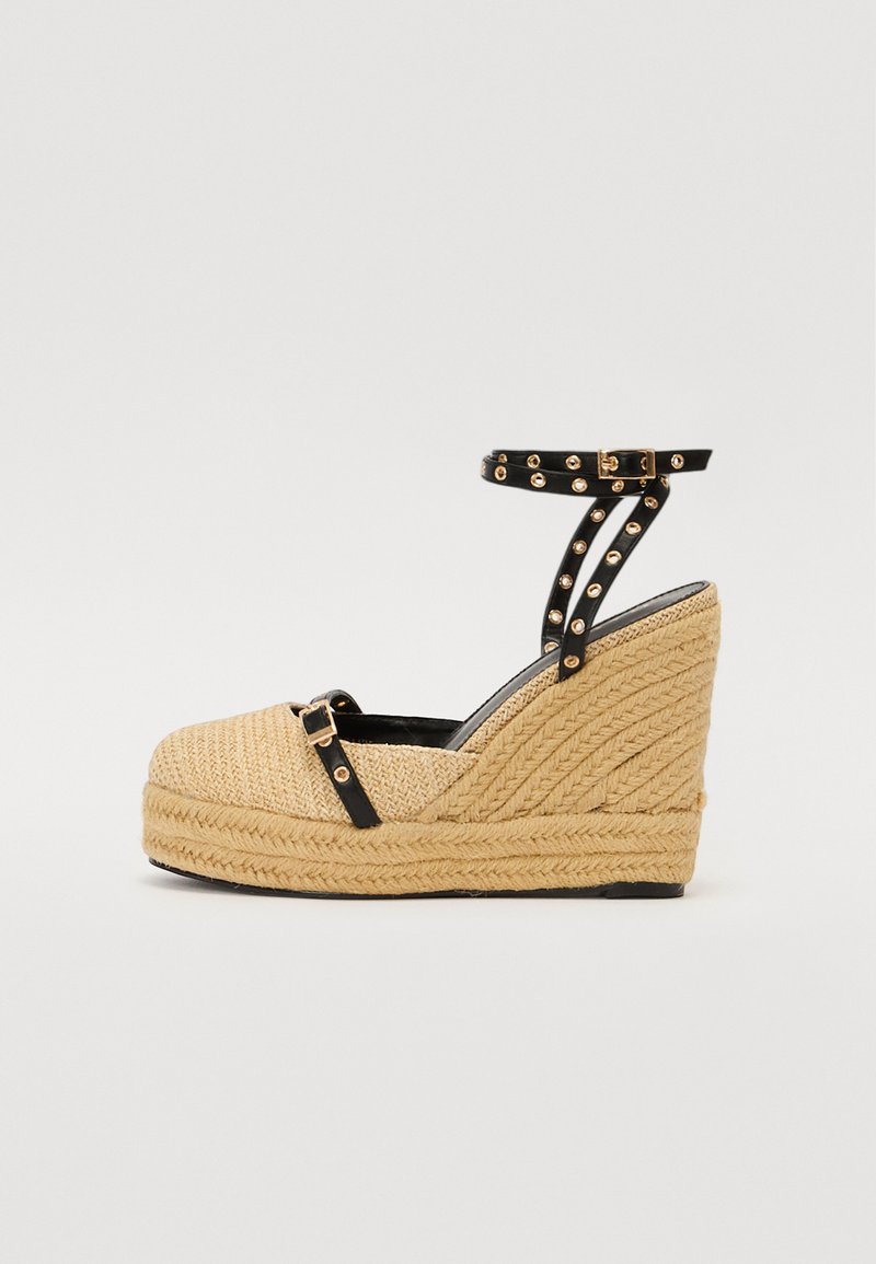Sandalias de plataforma cuña con un upper tejido en beige, correa negra en el tobillo con tachuelas doradas y detalles de cuerda texturizada en la suela.