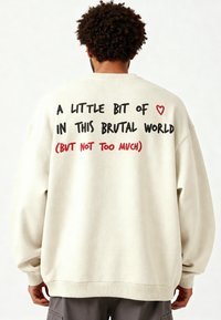 Felpa over-size color crema con maniche lunghe. Testo sul retro: "Un po' di ❤️ in questo mondo brutale (ma non troppo)."