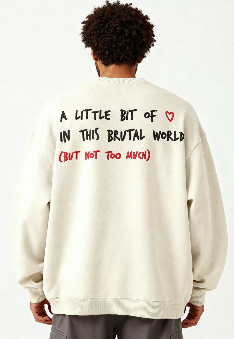 Felpa over-size color crema con maniche lunghe. Testo sul retro: "Un po' di ❤️ in questo mondo brutale (ma non troppo)."