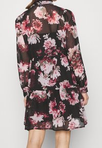 Robe fleurie avec un fond noir orné de grandes fleurs roses et blanches. Confectionnée en tissu transparent, manches longues, et design à plusieurs volants.