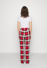 Punat, mustat ja valkoiset ruudulliset pyjamahousut, joissa on joustava vyötärö, näkyvät takaapäin valkoisen t-paidan kanssa. Sileä puuvillakudos.