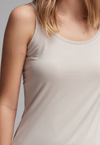 Débardeur beige clair en tissu doux et extensible. Il présente un col arrondi et des bretelles étroites, avec une texture lisse.