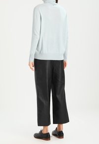 Helles blaues Rollkragensweatshirt mit gerippten Bündchen und Saum, kombiniert mit schwarzen, ledernen weiten Hosen und schwarzen Schnürschuhen.