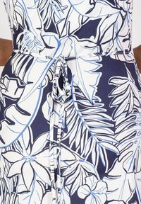 Marineblaues und weißes Kleid mit einem botanischen Druck in blauen Umrandungen. Strukturierter Stoff, Bindegürtel in der Taille und fließende Silhouette.