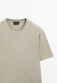 Beige bavlněné tričko s kulatým výstřihem a krátkými rukávy, s jemnou ribbenou texturou a značkovou nášivkou na vnitřním límci.