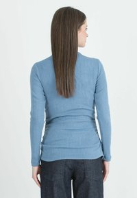 Top a maniche lunghe di un blu chiaro, a coste, con design aderente, scollo rotondo e dettagli arricciati sui lati, abbinato a pantaloni in denim scuro.