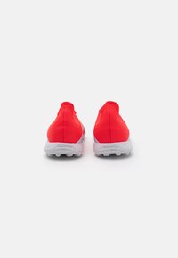Baskets de sport rouges avec un design élégant, un matériau texturé et une semelle en caoutchouc blanc avec des clous visibles, adaptées pour le sport.