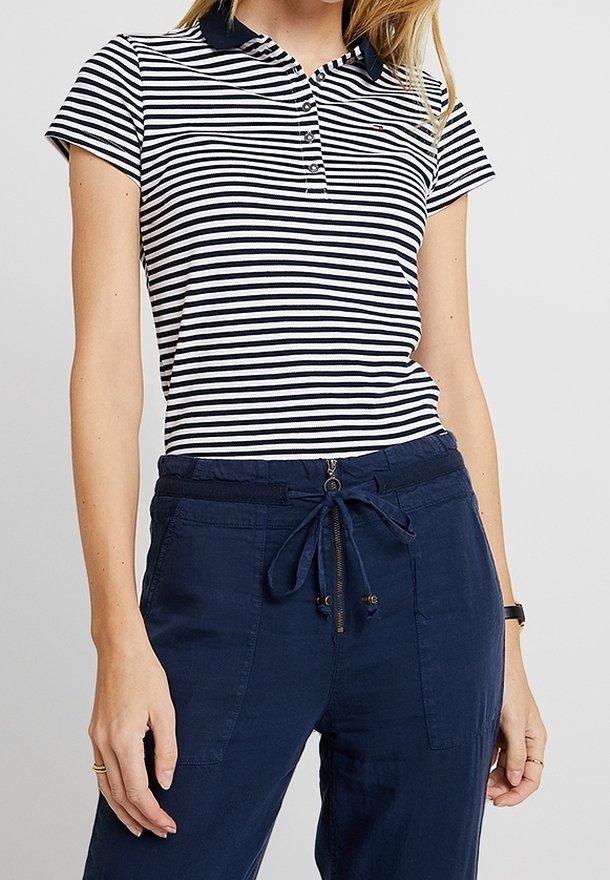 Femme portant un polo à rayures horizontales bleu marine et blanc à manches courtes et un pantalon bleu marine à cordon avec poches devant.