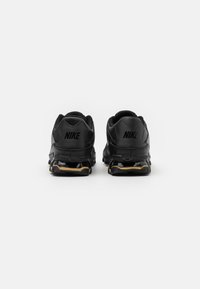 Sapatilhas Nike pretas com um superfície texturizada, apresentando um salto arredondado, sola acolchoada e detalhes dourados no solado.