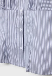 Gros plan sur une chemise rayée verticalement bleu et blanc avec des boutons blancs et une fente latérale à l'ourlet.