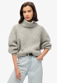Gray chunky knit sweater with a high collar, dropped shoulders, and rolled sleeves, paired with light blue high-waisted jeans.