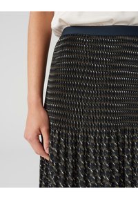 Jupe plissée avec un motif sombre présentant des formes géométriques en vert et blanc. Ceinture lisse ; tissu doux et texturé.