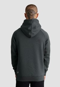 Felpa verde scuro con tasca a marsupio, polsini e orlo a costine, e un ampio cappuccio. Il materiale sembra morbido e con texture.