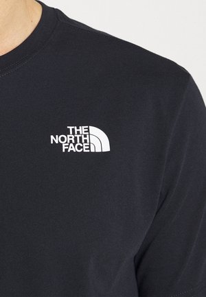 T-shirt noir avec logo blanc The North Face sur le côté gauche de la poitrine porté par une personne, montrant la zone du cou et des épaules.
