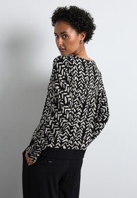 Schwarzer und weißer gemusterter Pullover mit lockerer Passform und weiten Ärmeln, der abstrakte Formen und einen gerippten Saum aufweist. Lässiges und strukturiertes Design.