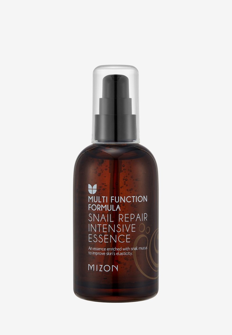 Brązowa szklana butelka z dozownikiem pompkowym, z białą etykietą tekstową. Zawartość wydaje się być ciekła, z widocznymi małymi bąbelkami powietrza.