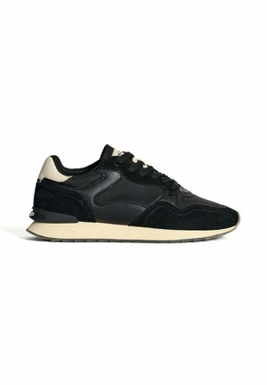 Baskets de sport noires en suède et cuir, avec une semelle beige et des accents texturés sur les côtés. Bout rond avec lacets.