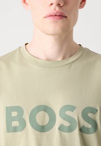 Zaļš kokvilnas t-krekls ar lielu "BOSS" tekstu tumšākā zaļā krāsā. Ar apaļu kakla dizainu un īsām piedurknēm, tam ir gluda tekstūra.