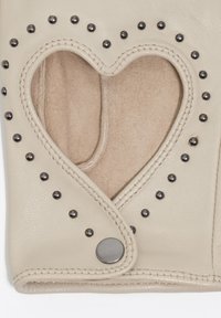 Guante de cuero beige con un recorte en forma de corazón, acentuado con tachuelas negras a lo largo de los bordes y un cierre de botón a presión. Forro interior suave visible.