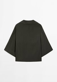 Vêtement d'extérieur léger vert foncé à manches courtes, avec un large col plat et un dos ouvert, présentant une texture lisse.