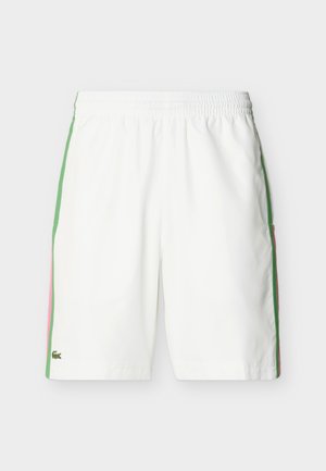 Valged spordipüksid elastse vöökohaga, roheliste ja roosade küljeribadega ning väikese rohelise krokodillilogo vasaku äärise lähedal.