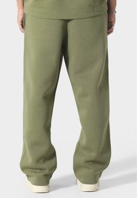 Housut oliivinvihreät, rentoa leikkistä, valmistettu pehmeästä materiaalista. Niissä on sivutaskut ja nauhakujat, ja ne on yhdistetty kermaisiin kenkiin.