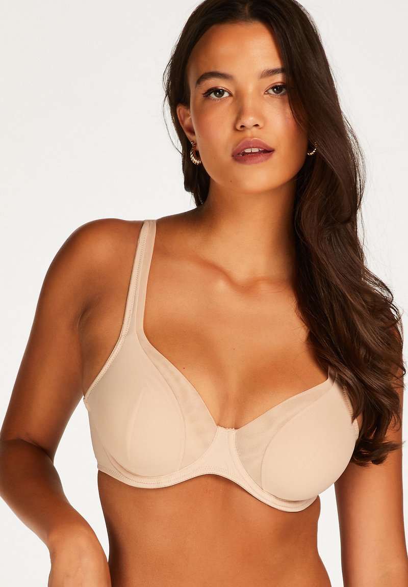 Beige onderwired bh van gladde stof, met een diepe halslijn, verstelbare bandjes en een ronde cupvorm met naadloze randen.