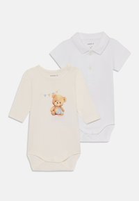 Två babyskydd: en beige med en nallebjörnsgrafik och vimpel, och en vit polo-stil med krage och knappdetalj.