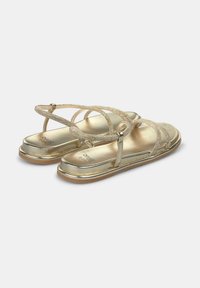 Gouden sandalen met een platte zool, voorzien van kruislings geplaatste banden van textuurmateriaal. Gladde afwerking met een subtiele glans, minimale details.