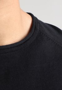 T-shirt en coton noir avec une texture lisse, doté d'un col rond et de coutures apparentes le long de la couture d'épaule.