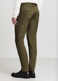 Olivgrüne Hose mit schlanker Passform aus glattem Stoff. Verfügt über zwei Gesäßtaschen und wird mit glänzenden schwarzen Schuhen kombiniert.