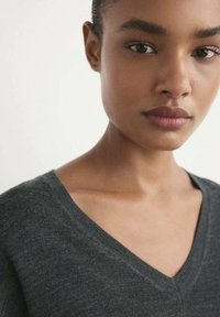 Pull en V gris foncé en matière douce, au design simple et à la texture tricotée fine, avec une coupe légèrement décontractée autour du cou.